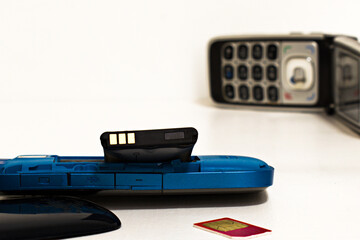old disassembled push-button telephone with damaged swollen battery on blurred background of another push-button phone