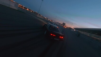 Fast sports jdm cars drift follow race driving about special ground near modern building against illuminated city in evening first point view fpv sport drone cinematic shot.