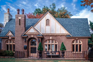 Charming brick vintage cottage with autumn colors and a Halloween skeleton on a bench outside front door - arched windows and door