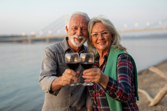 Portrait of happy elderly couple drinking wine on the riverside and toasting. 