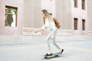 Professional woman with a backpack arriving to her work building in a skateboard