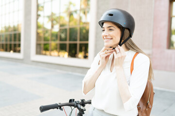 Happy adult woman fastening her helmet before a bike commute to her home