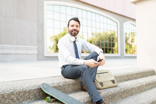 Portrait of an active man with a business outfit sitting with a skateboard