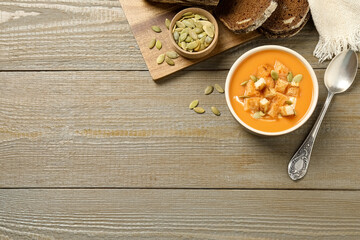 Obraz na płótnie Canvas Tasty creamy pumpkin soup served with bread and seeds on wooden table, flat lay. Space for text