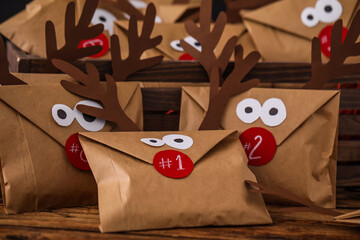 Gifts in envelopes with deer faces on wooden table, closeup. Christmas advent calendar