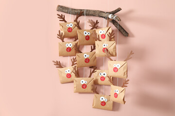 Gifts in envelopes with deer faces hanging on pink wall. Christmas advent calendar