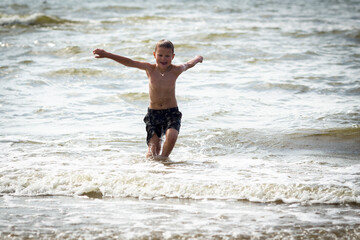 Young cheerful boy having fun at sea waves.