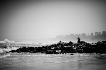 People sitting among waves breaking on rocks 
against the backdrop of the city at the  Chorrillos beach at Lima, Peru- 1 May 2015