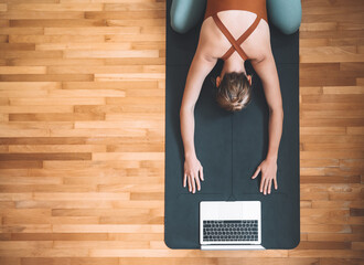 Top view of woman practicing yoga on yoga mat with laptop.