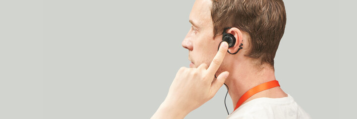 Men in call center. White t-shirt. Headset for telemarketing. Male manager helps customer. Phone operator. Studio portrait. Person multi language translator. Grey background. Earphones