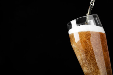 Pouring cold tasty beer into glass on black background, closeup. Space for text