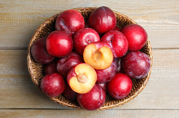 Delicious ripe plums in wicker bowl on wooden table, top view