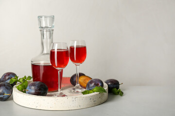 Delicious plum liquor, mint and ripe fruits on light table. Homemade strong alcoholic beverage