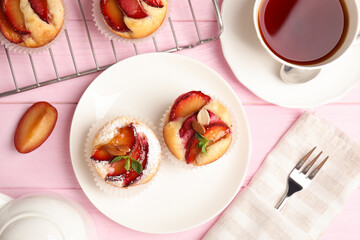 Delicious cupcakes with plums on pink wooden table, flat lay