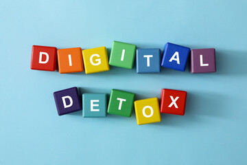 Colorful cubes with phrase DIGITAL DETOX on light blue background, flat lay