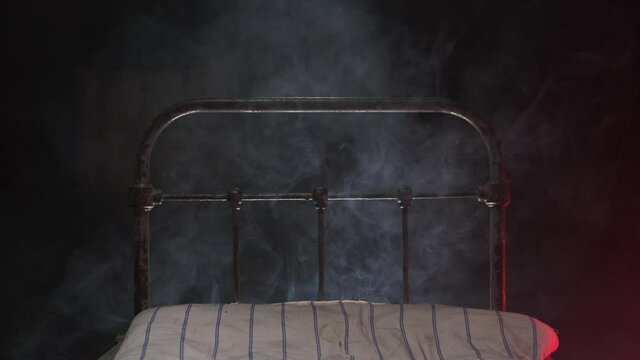 metal scary bed in mental hospital sinister in dark night with ghosts. White smoke around place for violent patients and corpses in prison or dark hospital with white old mattress.