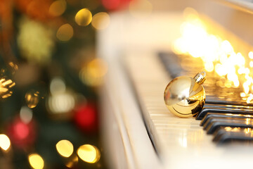 Beautiful golden bauble and fairy lights on piano keys, space for text. Christmas music