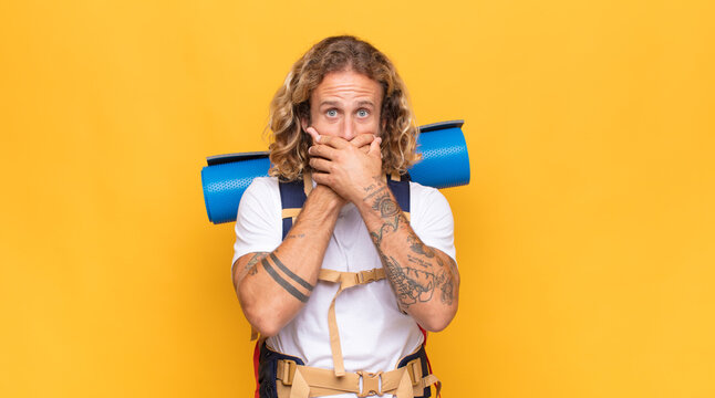 blonde man covering mouth with hands with a shocked, surprised expression, keeping a secret or saying oops