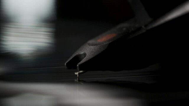 Extreme close-up of the head from a vinyl record player on a black record at night. Vintage or retro player for old timeless music hits of any century. Macro video of the music player.