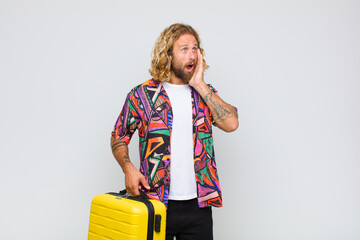 blonde man feeling happy, excited and surprised, looking to the side with both hands on face