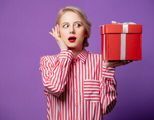 Beautiful woman in red striped shirt with gift box on purple background