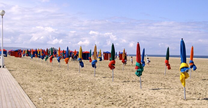 Parasols And People At Beach Against Cloudy Sky
