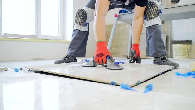 industrial tiler Professional builder worker installing floor a large ceramic tile at repair renovation work. Man experienced repairman laying placing tile indoors house or apartment. Finishing works