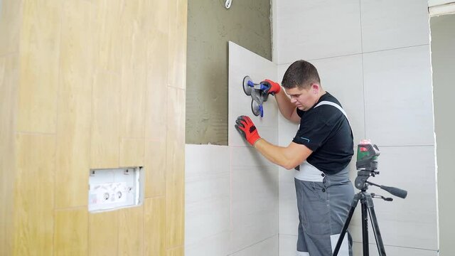 Male worker professional master laying ceramic tiles on the wall in the bathroom. Portrait experienced repairman man placing large size tiles. builder installing tile at repair renovation work