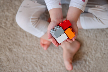 A small child holds in the palms of the rainbow construction blocks. Kid hands with bricks toy on beige background. Colorful educational toys. Flatlay. Buildings future. Copy space. Top view, postcard