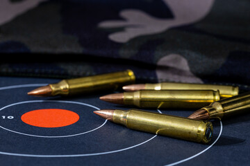 Loose rounds of rifle ammunition scattered on top of a paper target with a camouflage background. Background and foreground blurred with a shallow depth of focus. - obrazy, fototapety, plakaty