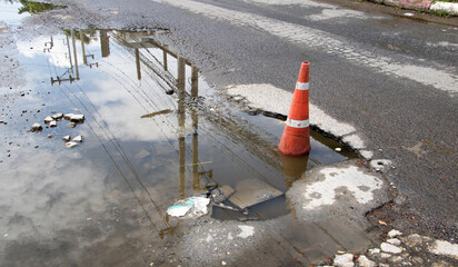 The concrete road is damaged, potholes, and waterlogged due to rain, so a  traffic cone is used to...