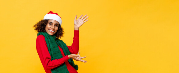 Cheerful happy woman in Christmas attire smiling and raising hands up to copy space in yellow banner isolated background