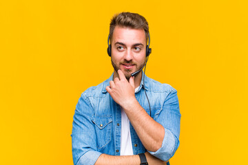 young man smiling with a happy, confident expression with hand on chin, wondering and looking to...