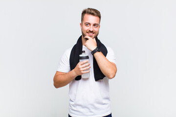 young man smiling with a happy, confident expression with hand on chin, wondering and looking to...