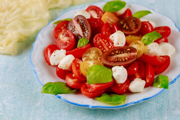 Tomato salad with mozzarella cheese and basil on blue background.