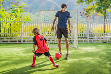 Little cute kid boy in red football uniform and his trainer or father playing soccer, football on field, outdoors. Active child making sports with kids or father, Smiling happy boy having fun in