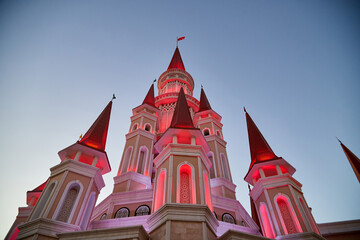 Night view of the high towers of the castle with pink illumination against the blue sky.