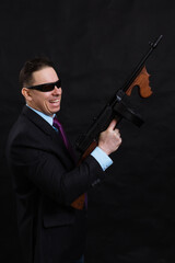Mature gangster in sunglasses dressed in suit with tommy gun