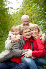 Naklejka na ściany i meble Grandmother and grandfather walking with adult children in nature. Mature couple and young couple walking in the park in an autumn day. Happy family outdoors.