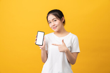 Cheerful beautiful Asian woman holding smartphone on light yellow background.