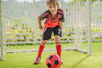 Little cute kid boy in red football uniform playing soccer, football on field, outdoors. Active...