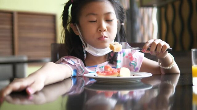 Asian girl kid eating with wear mask , ready for prevent corona virus and pm 2.5, new normal concept.
