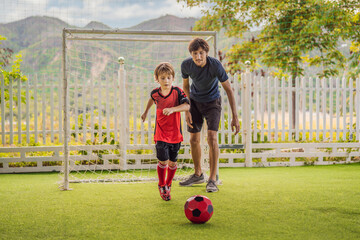 Little cute kid boy in red football uniform and his trainer or father playing soccer, football on field, outdoors. Active child making sports with kids or father, Smiling happy boy having fun in