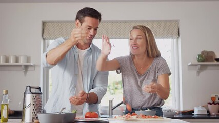 Couple at home in kitchen with man making as mess with toppings for homemade pizza - shot in slow motion