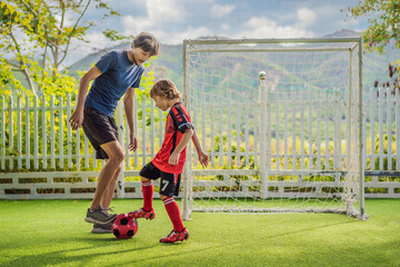 Little cute kid boy in red football uniform and his trainer or father playing soccer, football on field, outdoors. Active child making sports with kids or father, Smiling happy boy having fun in
