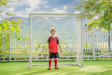 Little cute kid boy in red football uniform playing soccer, football on field, outdoors. Active child making sports with kids or father, Smiling happy boy having fun in summer
