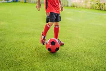 Obraz premium Little cute kid boy in red football uniform playing soccer, football on field, outdoors. Active child making sports with kids or father, Smiling happy boy having fun in summer