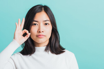 Young beautiful Asian woman smiling and showing hand the OK sign, Portrait female show finger okay gesture, studio shot isolated on a blue background