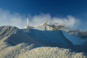 Facilities of mining industry against the background of a blue sky with a bunch of crushed stone in the foreground.