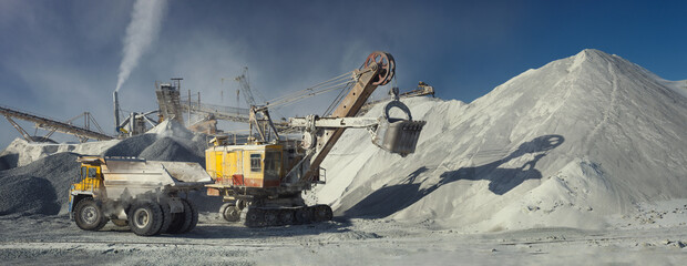 Mining excavator and mining dump truck on the background of the stone-crushing equipment of the mining enterprise, panorama. Industrial landscape. © esalienko
